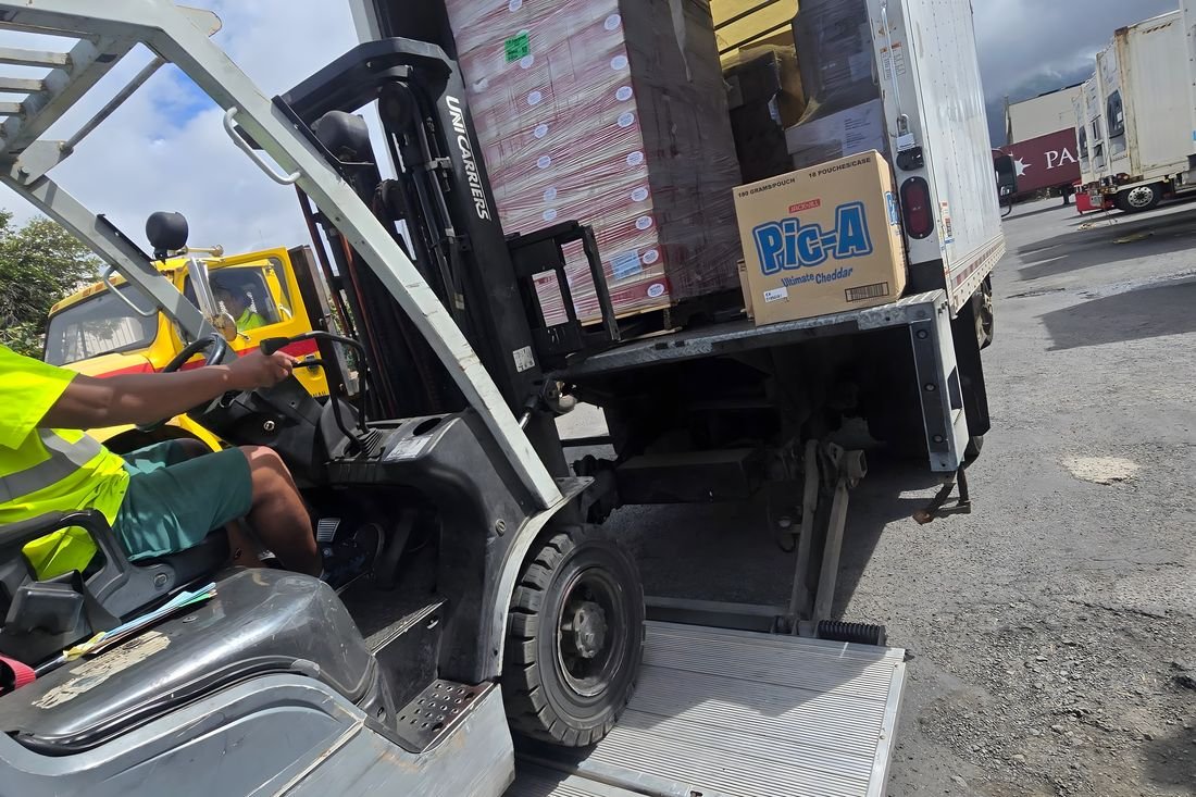 A forklift unloading pallets of boxes from a box truck