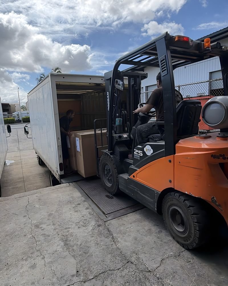 A forklift driver and a box truck at a loading area under a cloudy sky