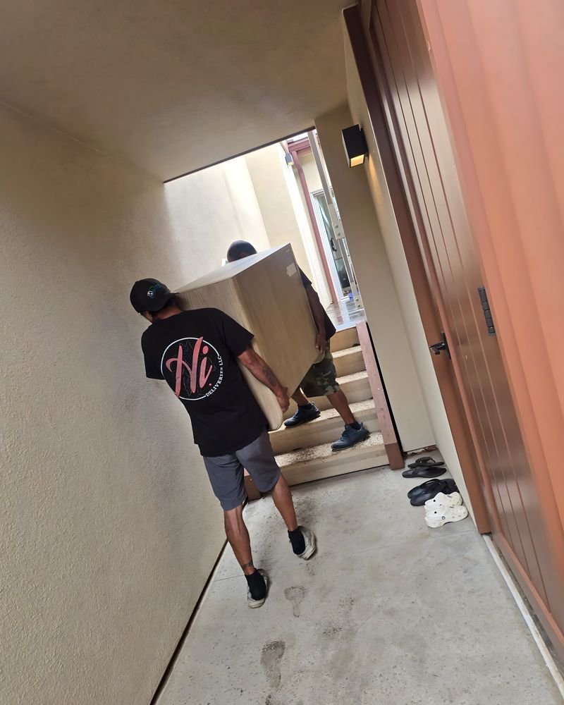 A crew member carrying a large boxed item through a hallway toward stairs