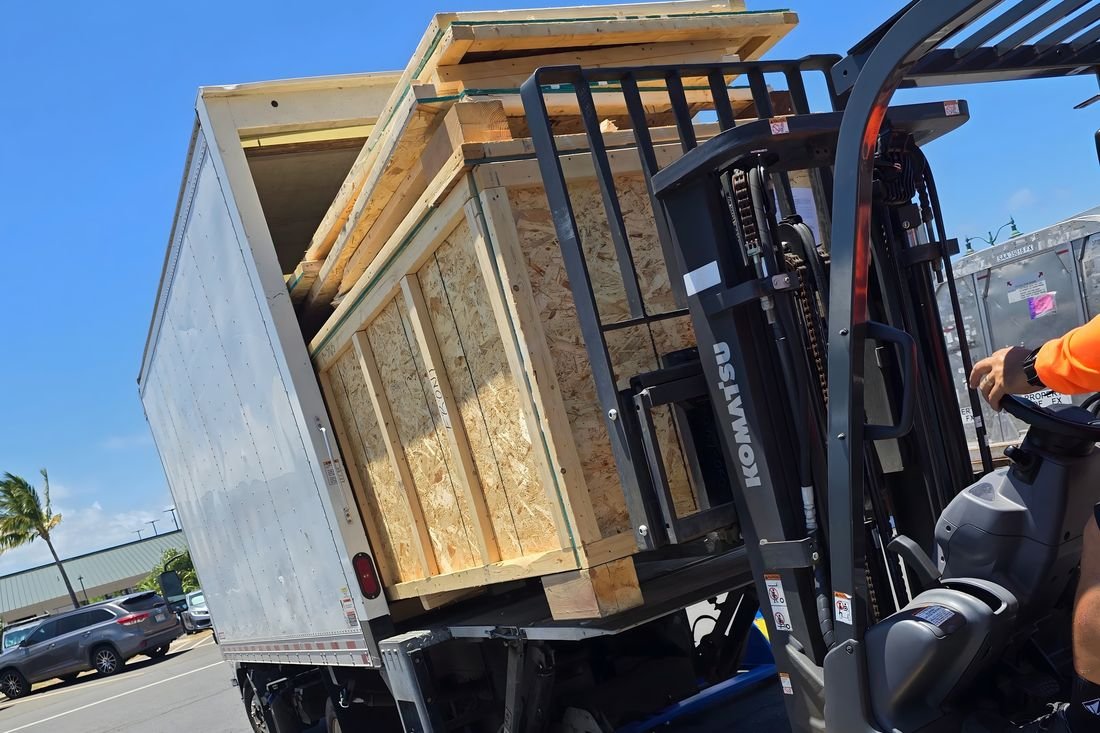 A forklift loading a large wooden crate onto a box truck